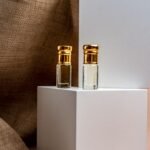 Close-up of two elegant perfume bottles with gold caps on a minimalist white display, evoking luxury.