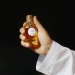 Close-up of a hand holding a luxurious perfume bottle against a dark background, capturing elegance.